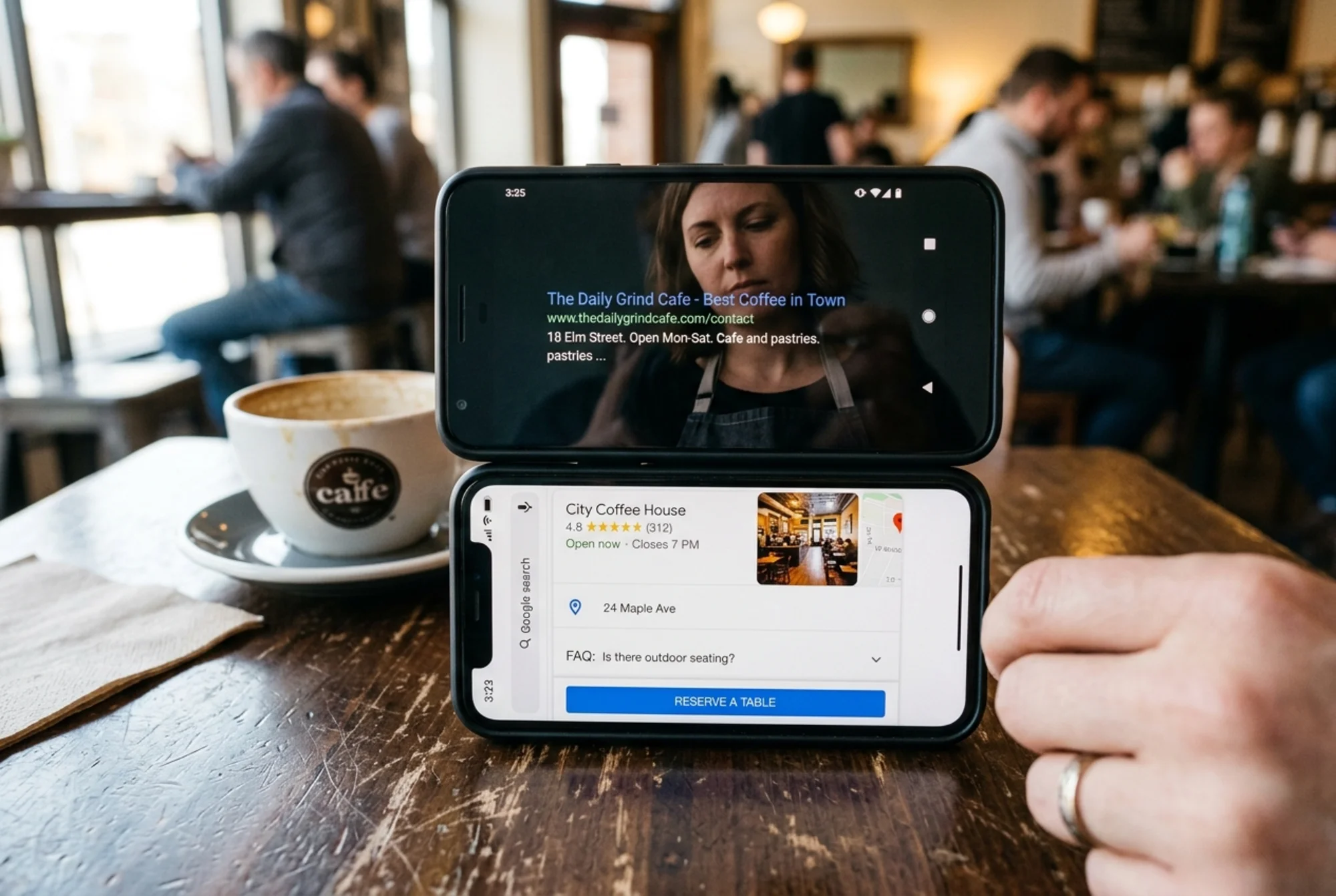 Side-by-side phone screens showing two Google search results for local cafes: the top is a plain blue link with just a title and URL, the bottom shows the competitor's listing with star ratings, hours, FAQ dropdown, and a "Reserve a table" button—frustrated cafe owner's reflection faintly visible in the screen