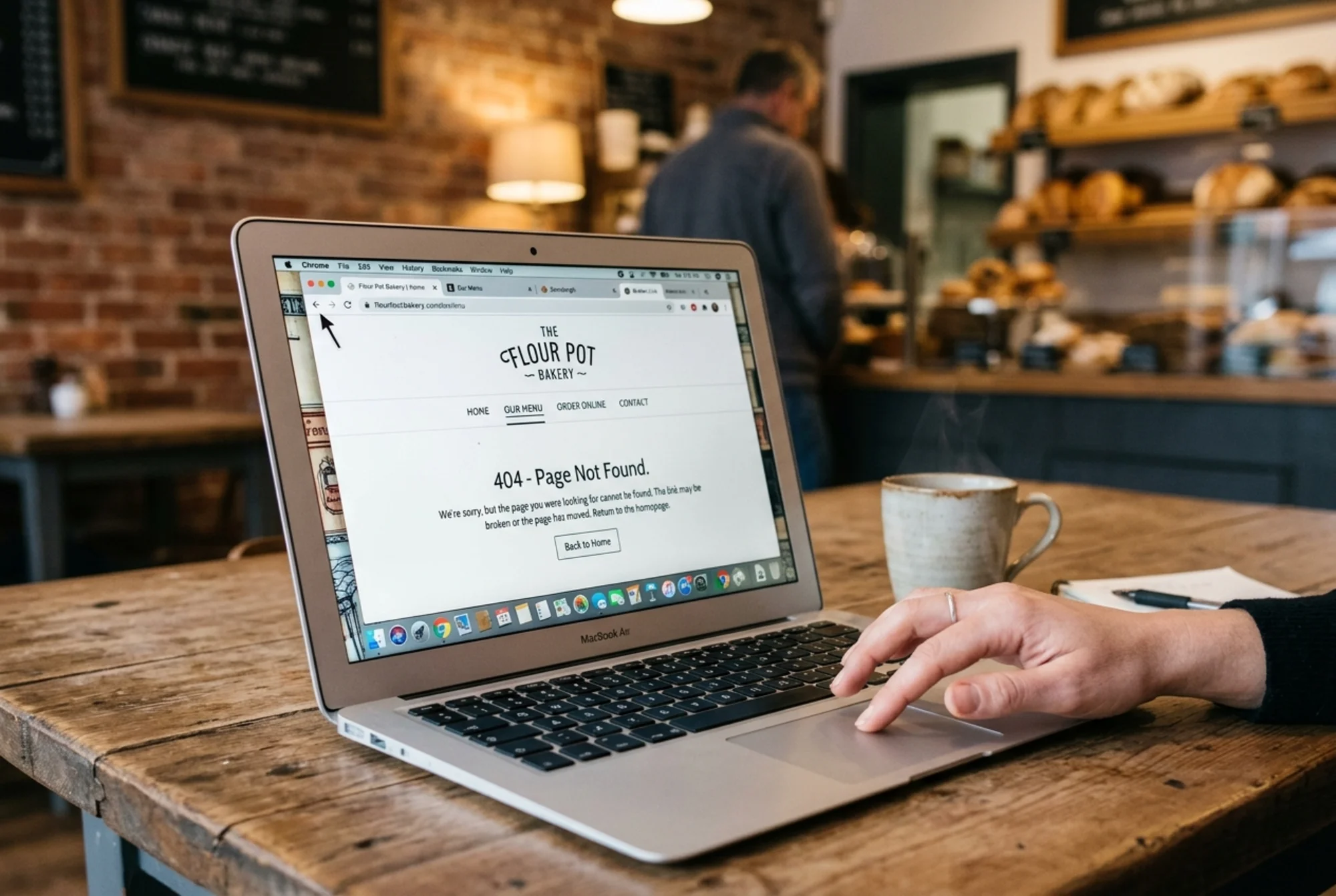 A laptop screen showing a small bakery website with a "404 Page Not Found" error after a customer clicked an internal menu link, browser tabs visible, slightly frustrated hand reaching for the back button, realistic web interface