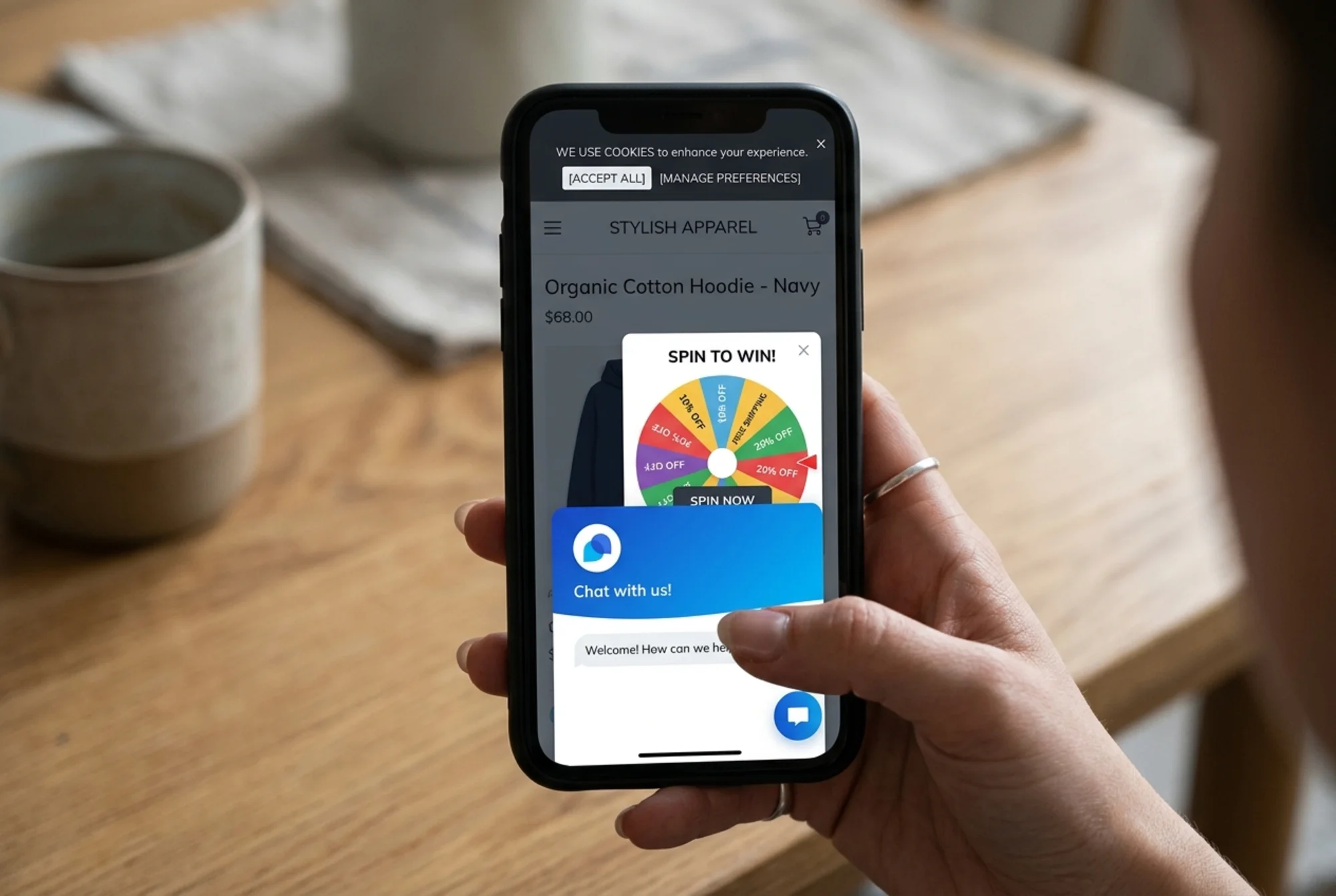 Mobile phone screen showing a Shopify product page nearly blocked by a stacked Tidio chat bubble, cookie banner, and discount wheel popup, with a frustrated shopper's hand holding the device